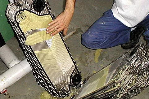Scambiatore di calore a piastre smontato per la pulizia, con piastre guarnite e residui di incrostazioni visibili